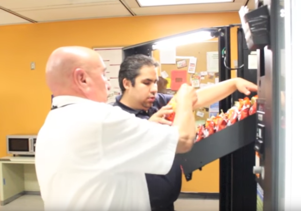 man helping another stock a vending machine